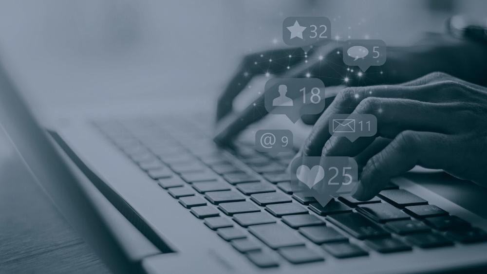 A person typing on a laptop with floating social media icons.